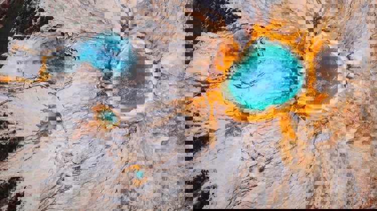 A drone image shows Yellowstone National Park from above with its vibrant blue and orange hot pools.